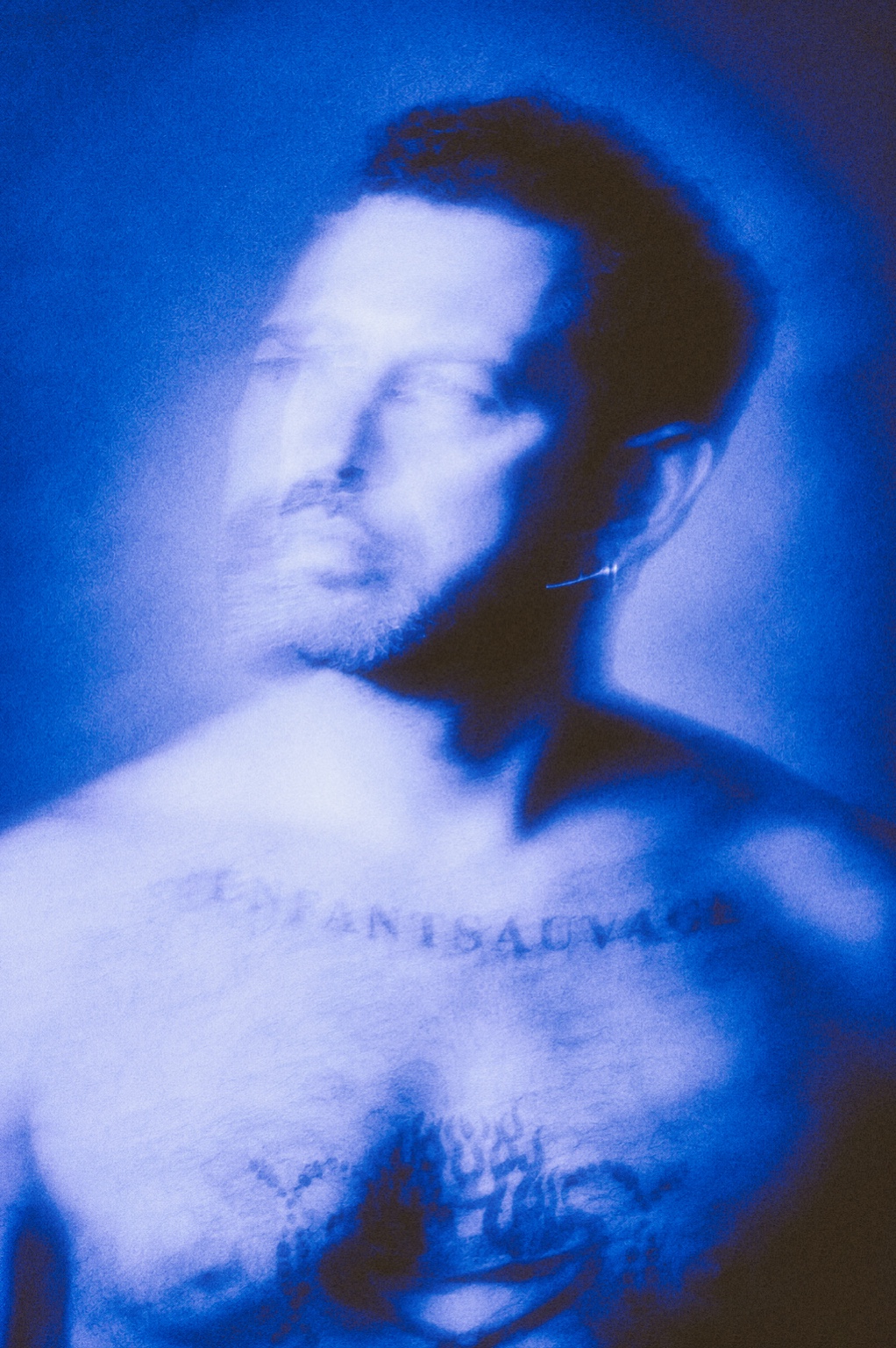 Ritratto di Giovanni Vitale in blu, con il volto mosso e il tatuaggio sul petto