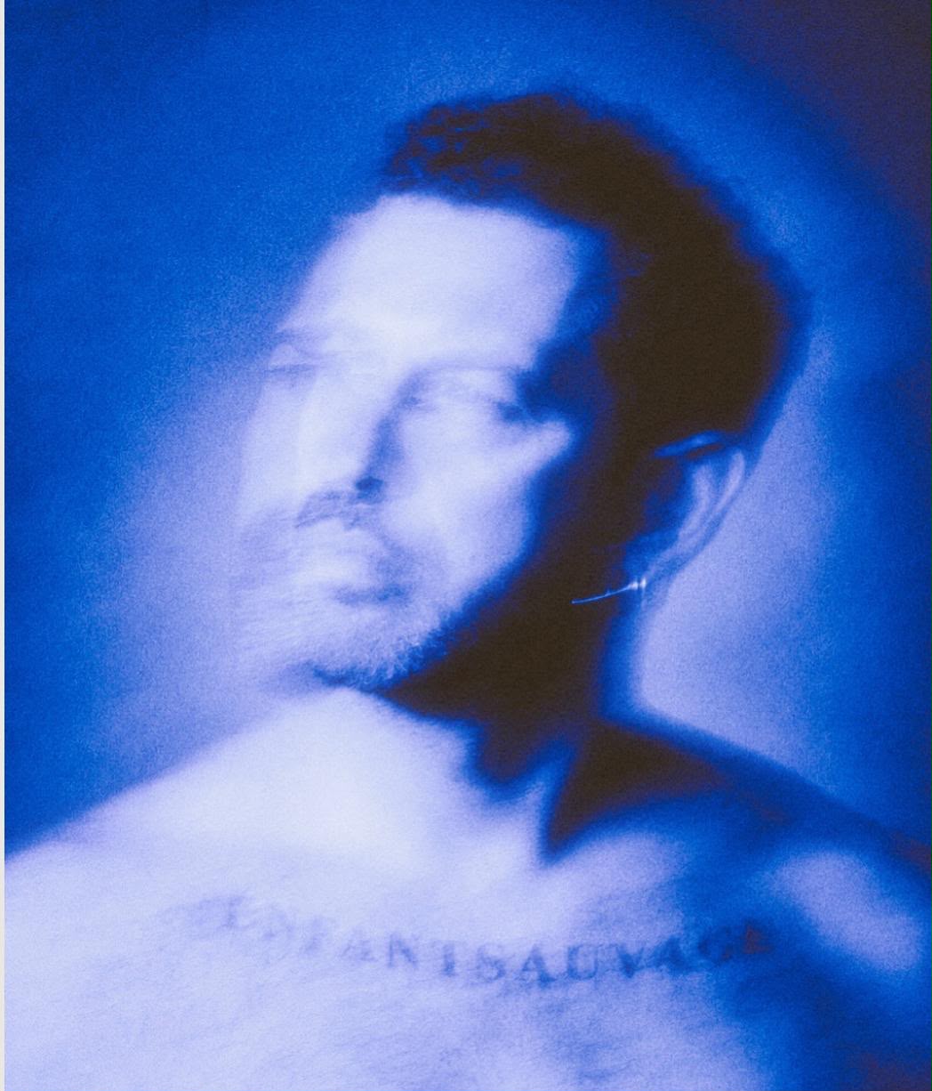 Ritratto di Giovanni Vitale in blu, con il volto mosso e il tatuaggio sul petto